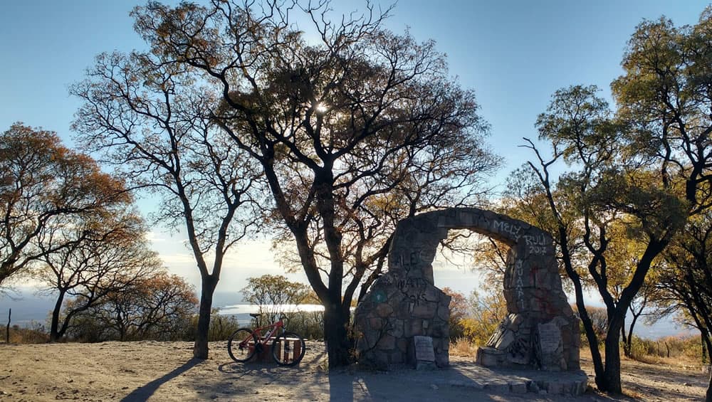 Arco de piedra graffiteado con bici al lado y árboles alrededor