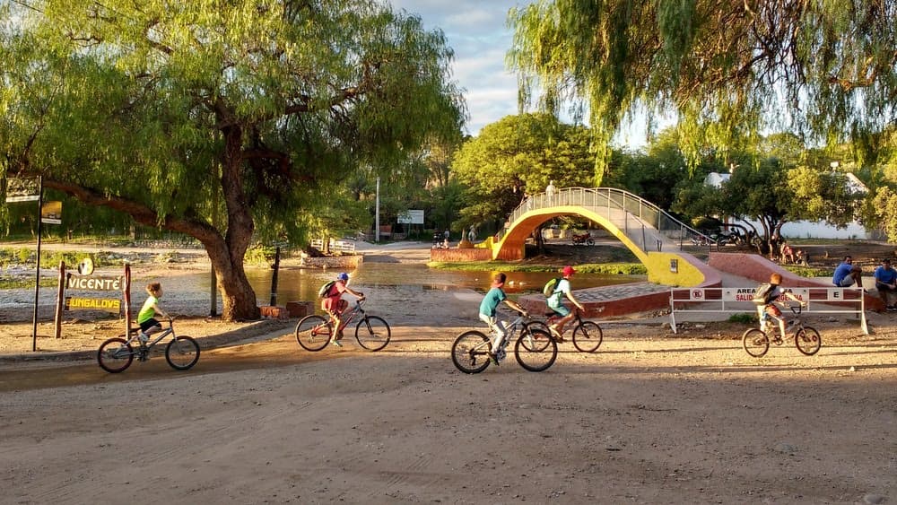 Calle con niños en bici y puente peatonal atrás