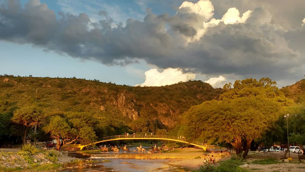 Puente peatonal con vegetación alrededor y las sierras de fondo